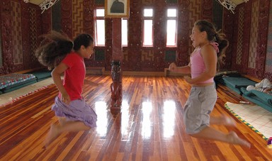 darius mccallum; two girls practising their dance moves; taken at a marae in glen eden, the girls' active exuberance juxtaposed by the unblinking gaze of the eyes on the wall