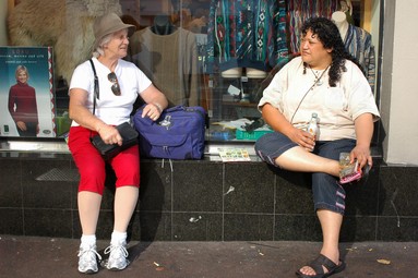  two women seated in a shop window sill, chatting while waiting for the bus to arrive, albert st. Auckland