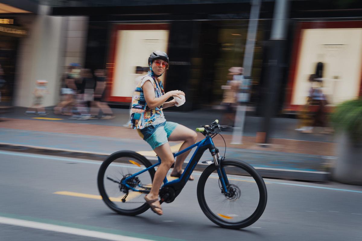 LEYAO LIU;Snack Time on Wheels;A candid shot of a woman enjoying some snacks while riding a bicycle in the busy streets of the CBD. The photo captures the contrast between her relaxed attitude and the hectic urban environment around her.
