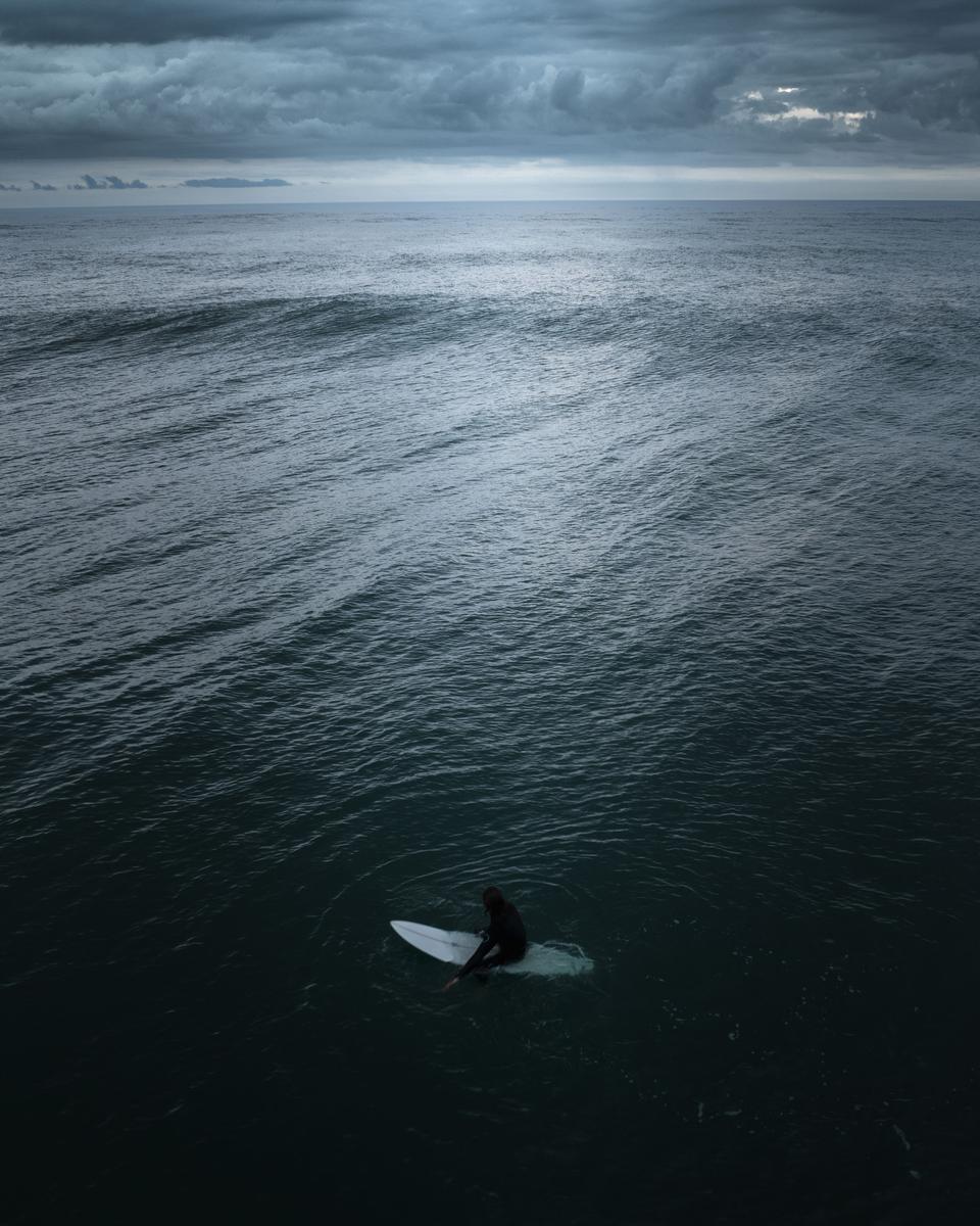 Tieshu Zhu;Eternal Anticipation;A lone figure perched upon the board, a surfer waits in anticipation, suspended between the calmness of the vast ocean and the imminent rush of adrenaline. The composition captures a moment of serene stillness, emphasizing the surfer's connection with the elements and the unwavering determination to ride the waves. Through this image, the essence of patience and the symbiotic relationship between humans and nature are poetically portrayed, inviting us to contemplate the anticipation and exhilaration that awaits us in life's unfolding moments.