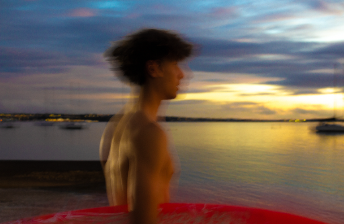 Indi Nicholas;Where the light leaves us;Captured mid motion, he drifts through the last light of day — a symbol of all we try to hold onto. There's warmth behind him, stillness around him, but his figure slips forward into the blur of what’s next. Sometimes, growing feels like fading. Sometimes, presence looks like absence. This is that quiet in between.