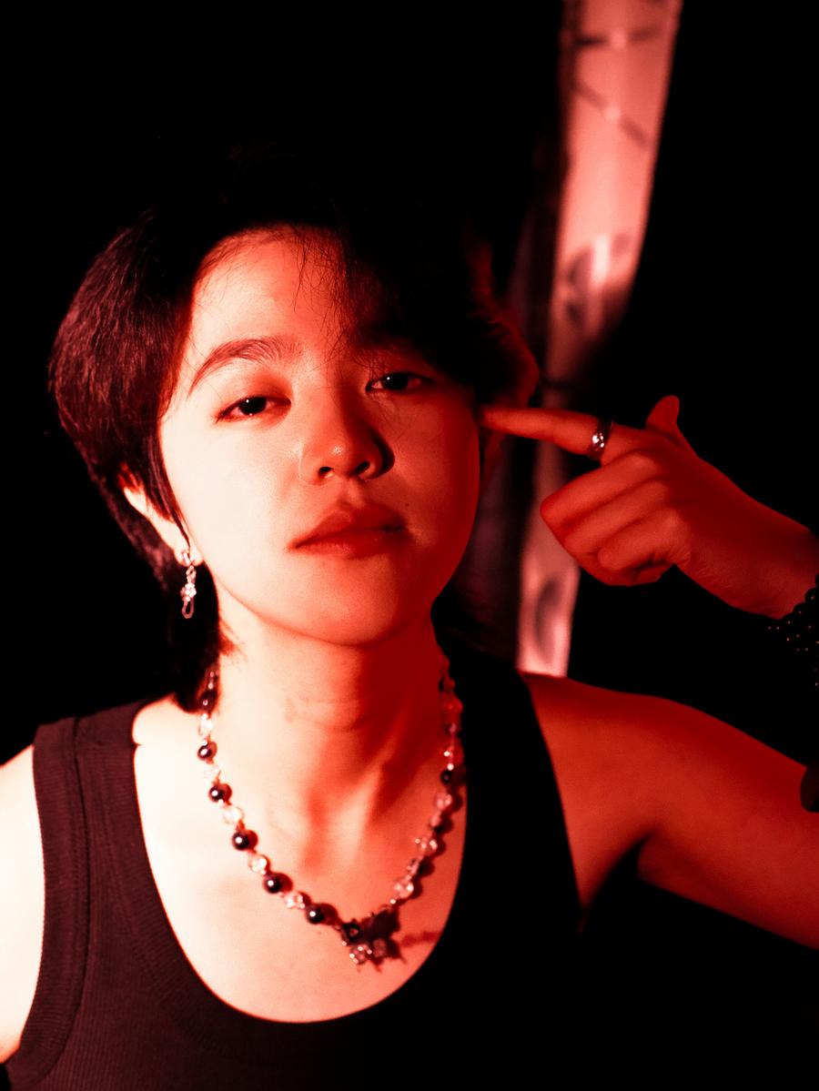 Jingjing Lyu;She Whispered Under Red Light;Bathed in crimson haze, her gaze blurs the line between defiance and desire. Fingers form a gesture, not of threat, but of metaphor — a silent dialogue with the self. She aims not at the world, but inward, where identity flickers like a neon confession.