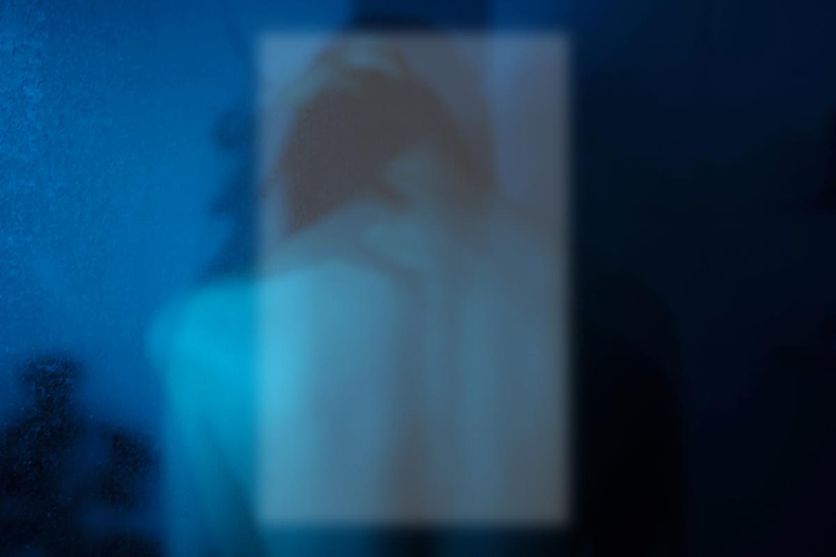 Sara Li;In the Square of Me;My work explores my self identity and emotional isolations. I’ve photographed my own silhouette through a semi opaque pane of glass, the blurred square at its center fragmenting my reflection. Bathed in cool blue tones, the image invites you to linger on the spaces between clarity and concealment, asking “Ko wai au? / Who am I?” The obscured form and subtle distortions symbolize how identity feels both visible and hidden, a layered self revealed only through reflection.